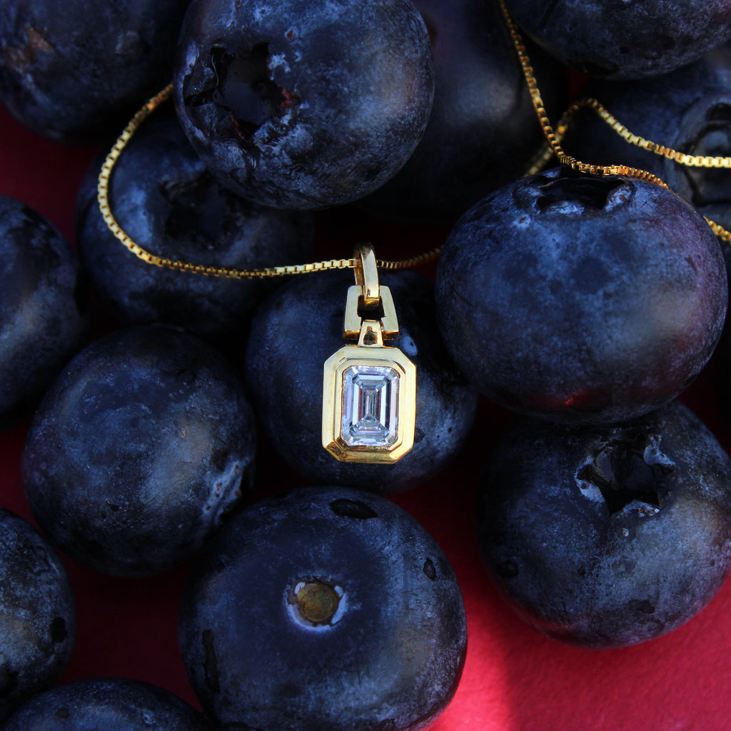 Gold necklace with a pendant on blueberries against a red background